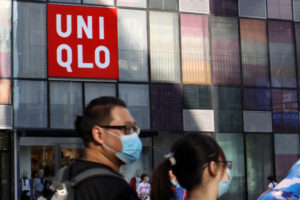 ユニクロのロゴマークが見える建物の前を通行するマスク着用の男性