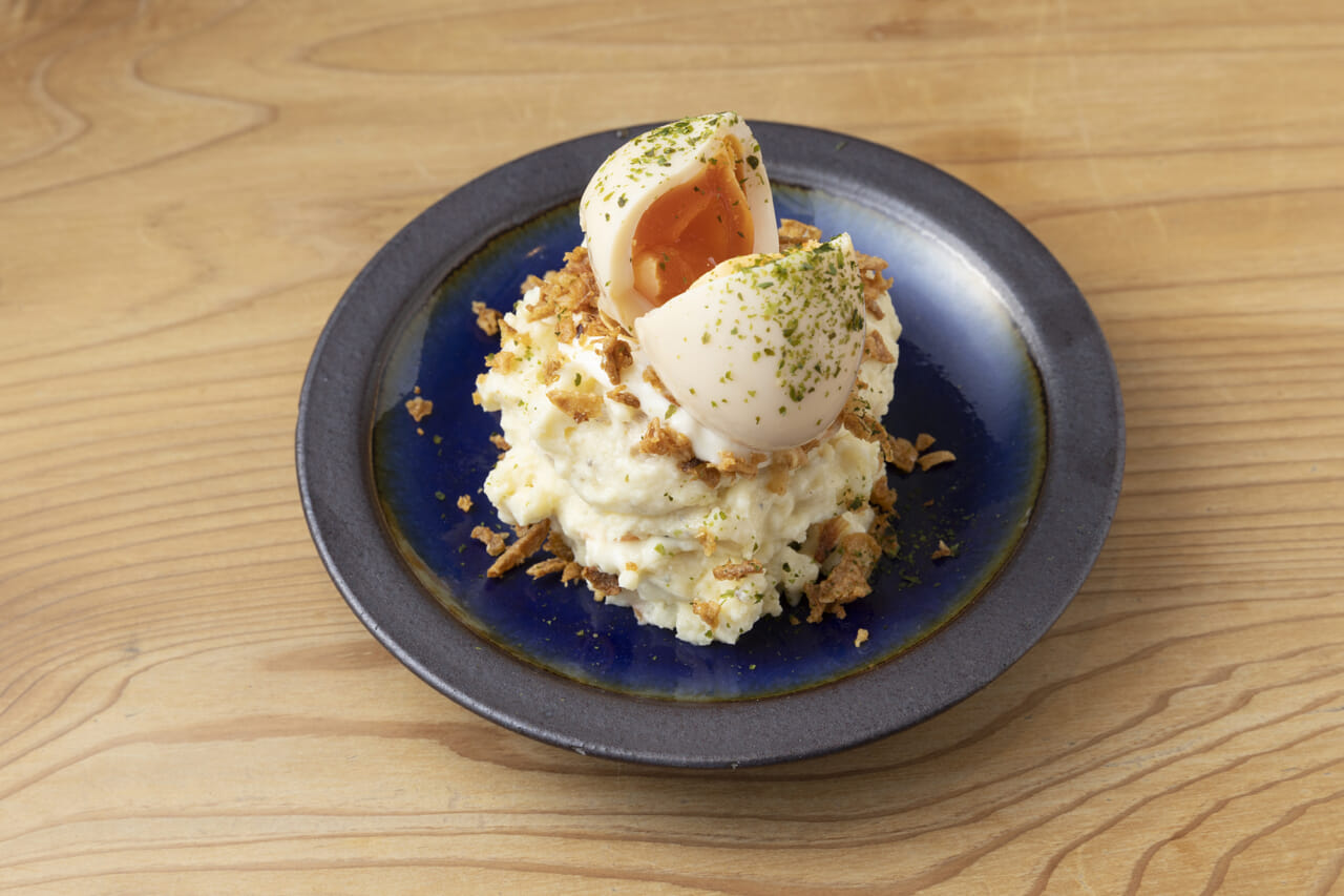 TOKIの卵ポテトサラダ550円。味玉をのせ、黄身がとろりと流れるシズル感を演出。明太子や卵、エビ、牛すじといった老若男女が好きな食材を多用