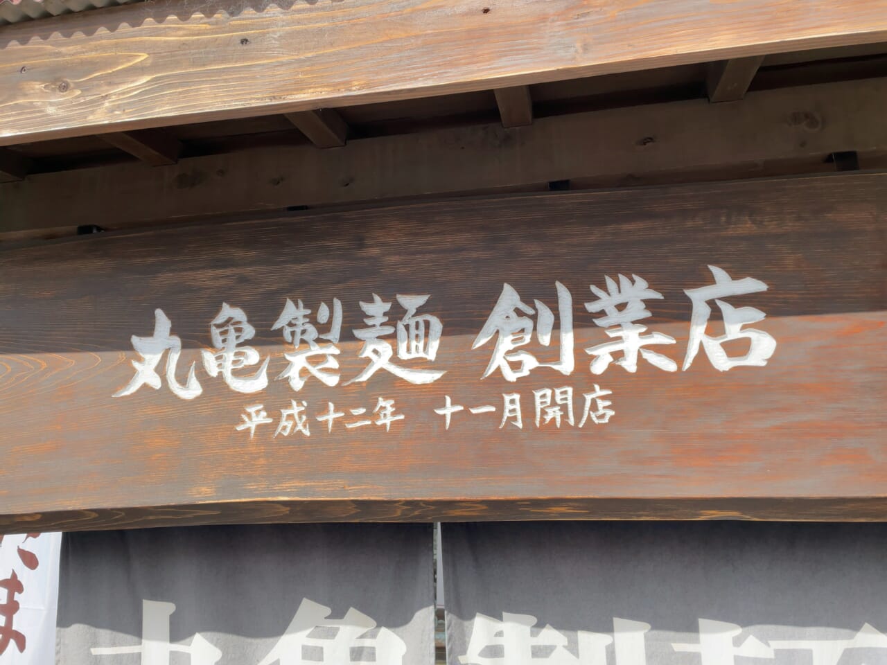 「丸亀製麺 創業店 平成十二年 十一月開店」と刻まれた木製の看板が誇らしい
